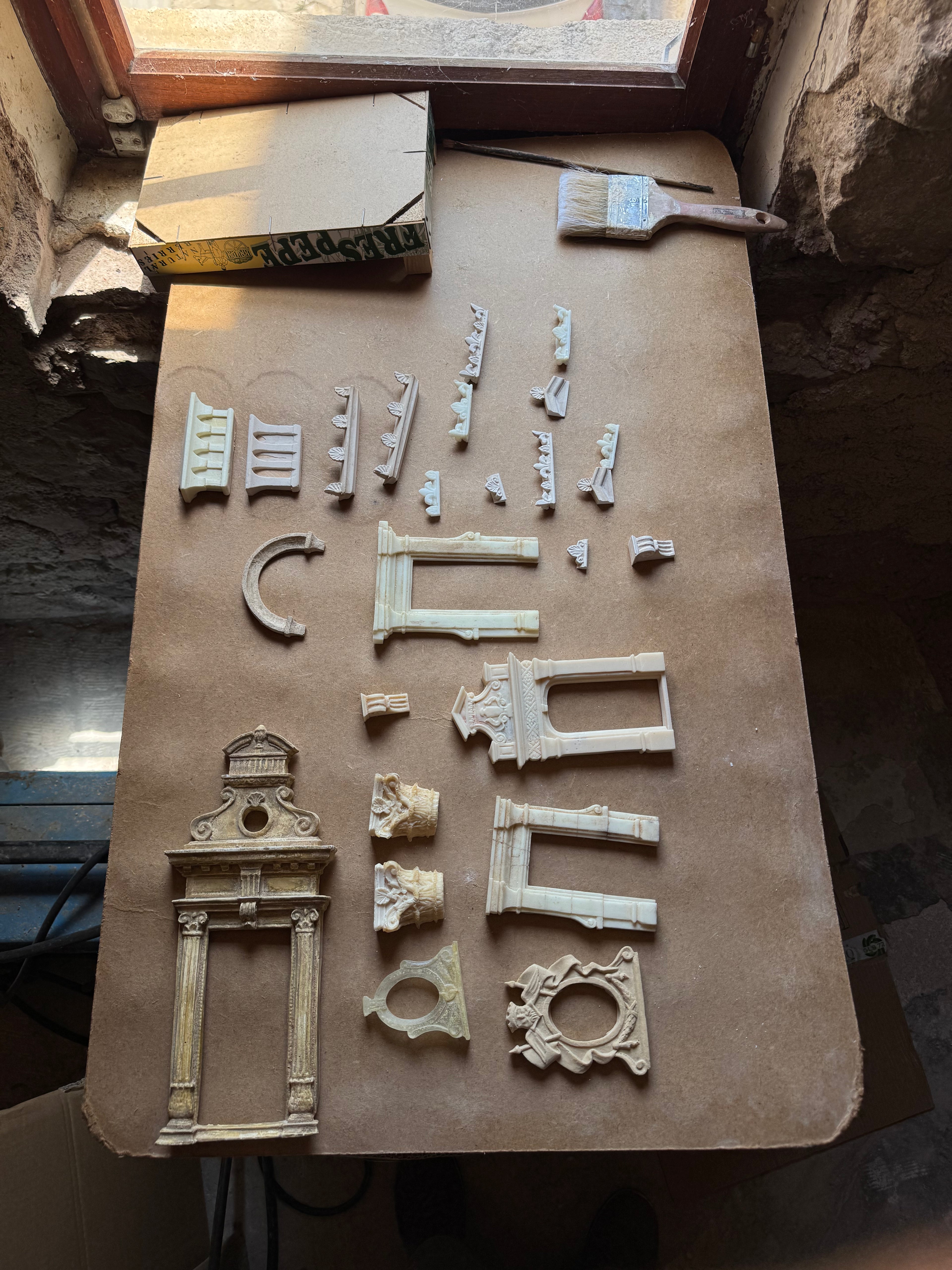 Hand-cast plaster architectural fragments—door surrounds, columns, balustrades and a sunburst ornament—arranged on a studio worktable in southern France