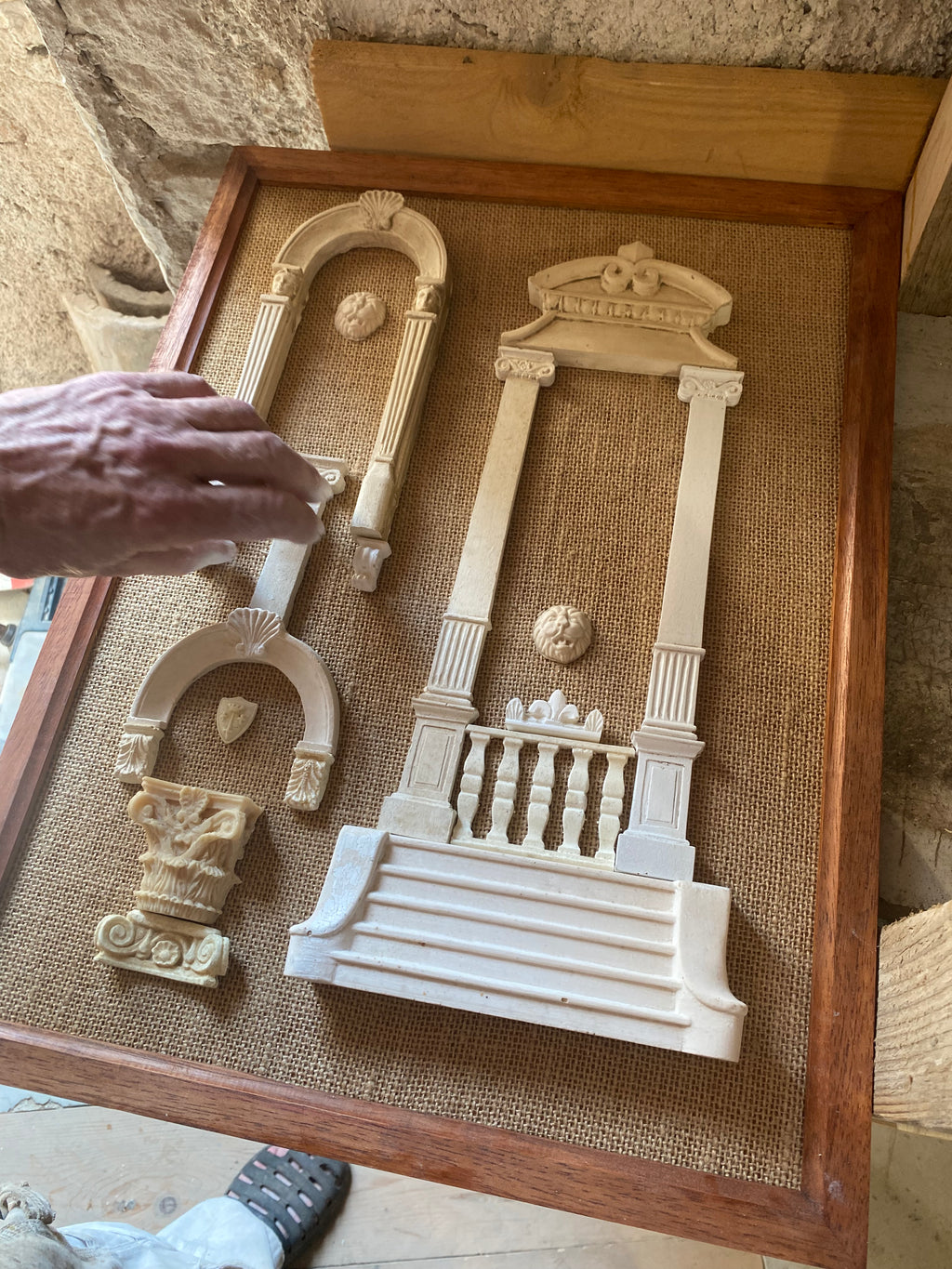 Eric Lansdown's hand arranging plaster columns, arches and a grand staircase on hessian during the making of a framed Architectural Archive panel